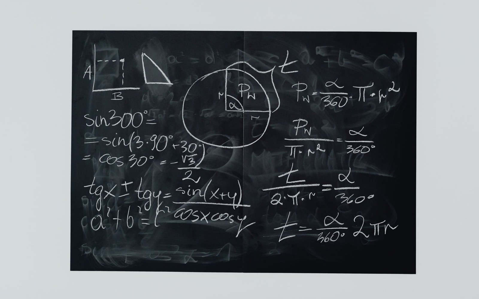 Chalkboard covered with trigonometry equations, circle geometry diagrams, and sector area formulas