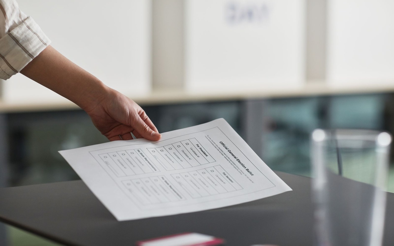 A hand places an official printed election ballot on a table