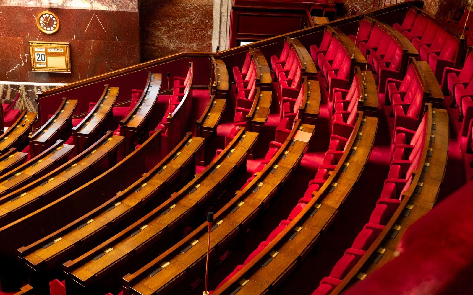 Empty curved rows of red seats and wooden desks in a parliamentary chamber