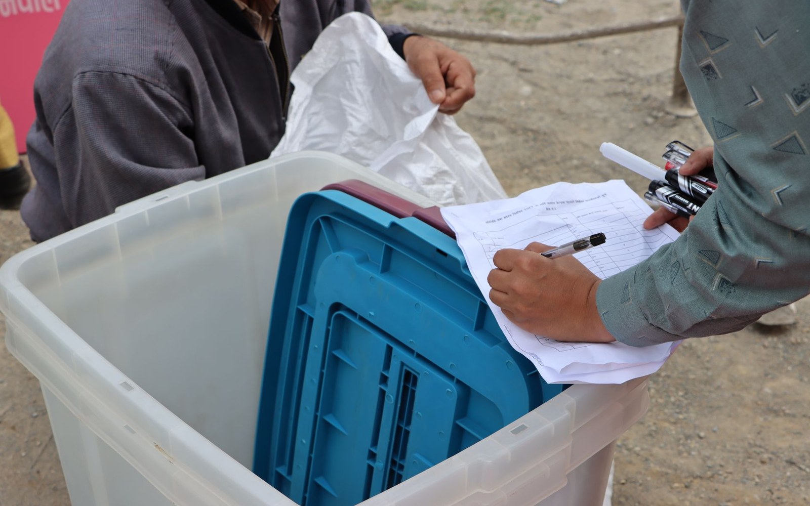 A person writes on a paper form beside a plastic bin holding blue storage boxes