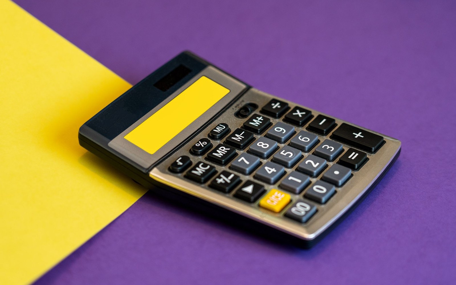 A calculator with a blank yellow display resting on yellow and purple paper backgrounds