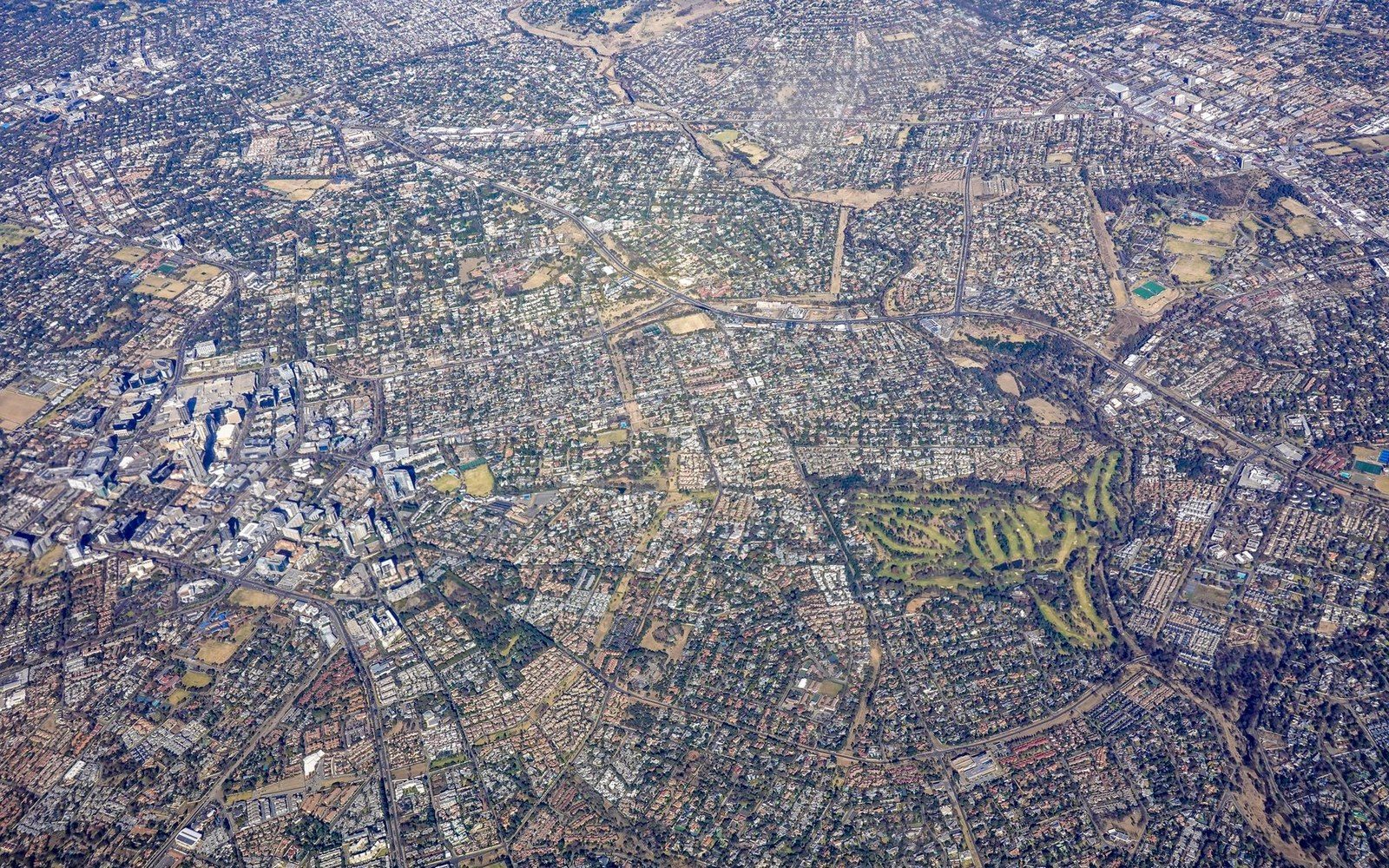 Aerial view of dense suburban neighborhoods, roads and a golf course stretching to the horizon