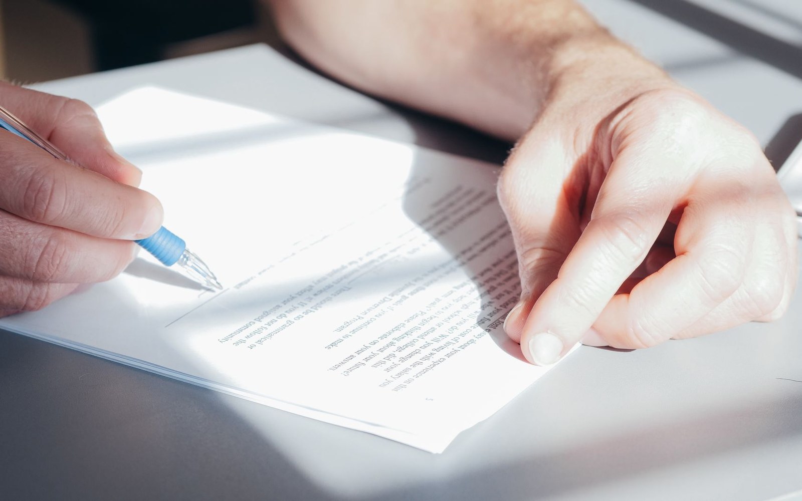 A hand holding a pen prepares to sign a printed document on a desk
